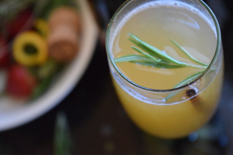 Close-up of a yellow cocktail garnished with rosemary in a clear glass.